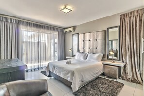 A modern bedroom with a large bed, a bedside table with a lamp, a mirror, and a view of the outdoors through sheer curtains. - Heritage Square Apartments (Cape Town)