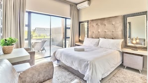 A modern bedroom with a large bed, a bedside table, a chair, a small table with a plant, and a balcony with a view. - Heritage Square Apartments (Cape Town)