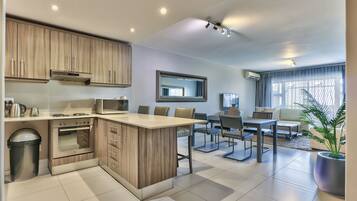A modern kitchen with an island, built-in oven, and microwave. There is a dining area with a table and chairs, and a large window with curtains.