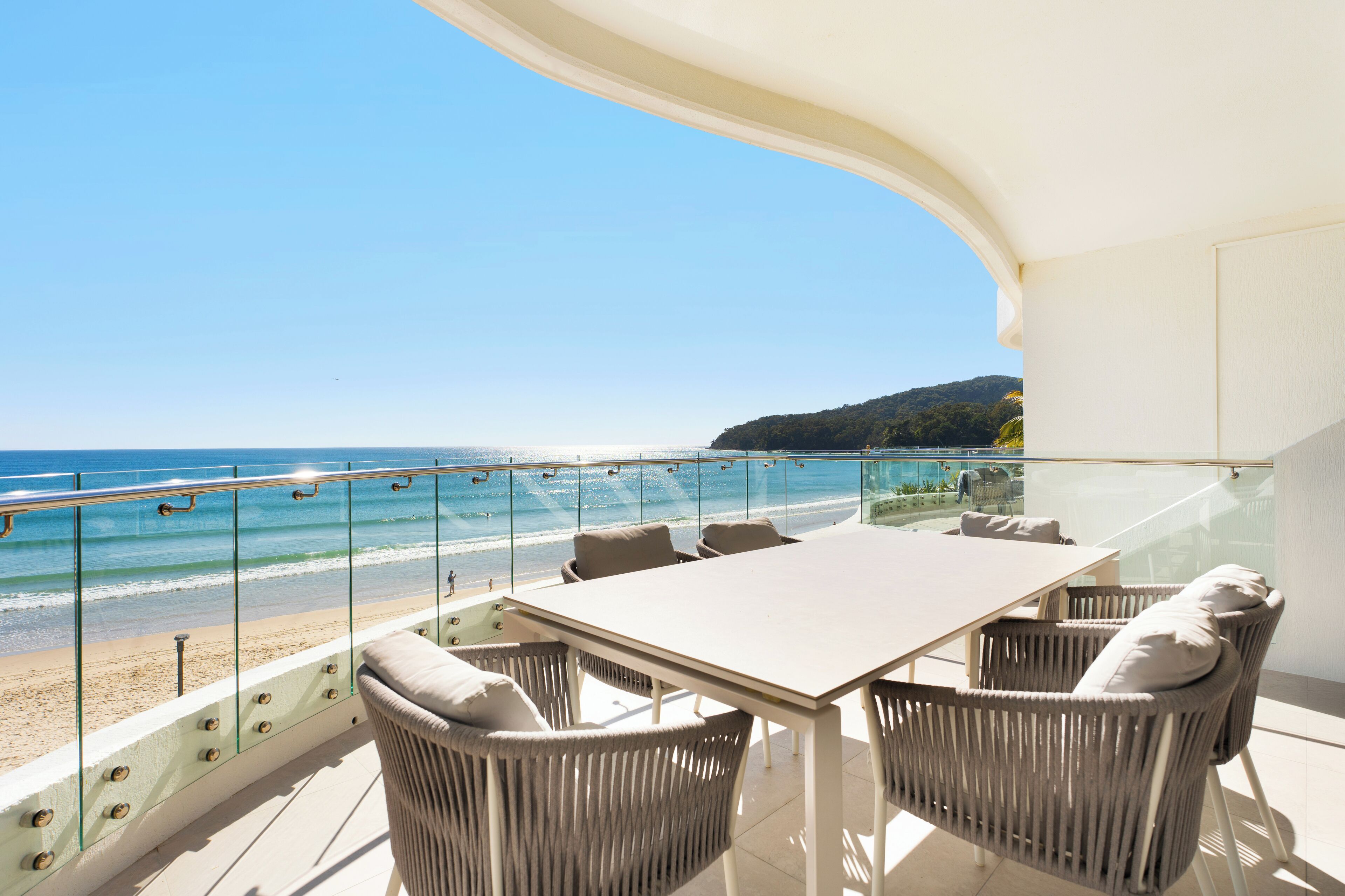 A balcony with a glass railing overlooking a beach and ocean.