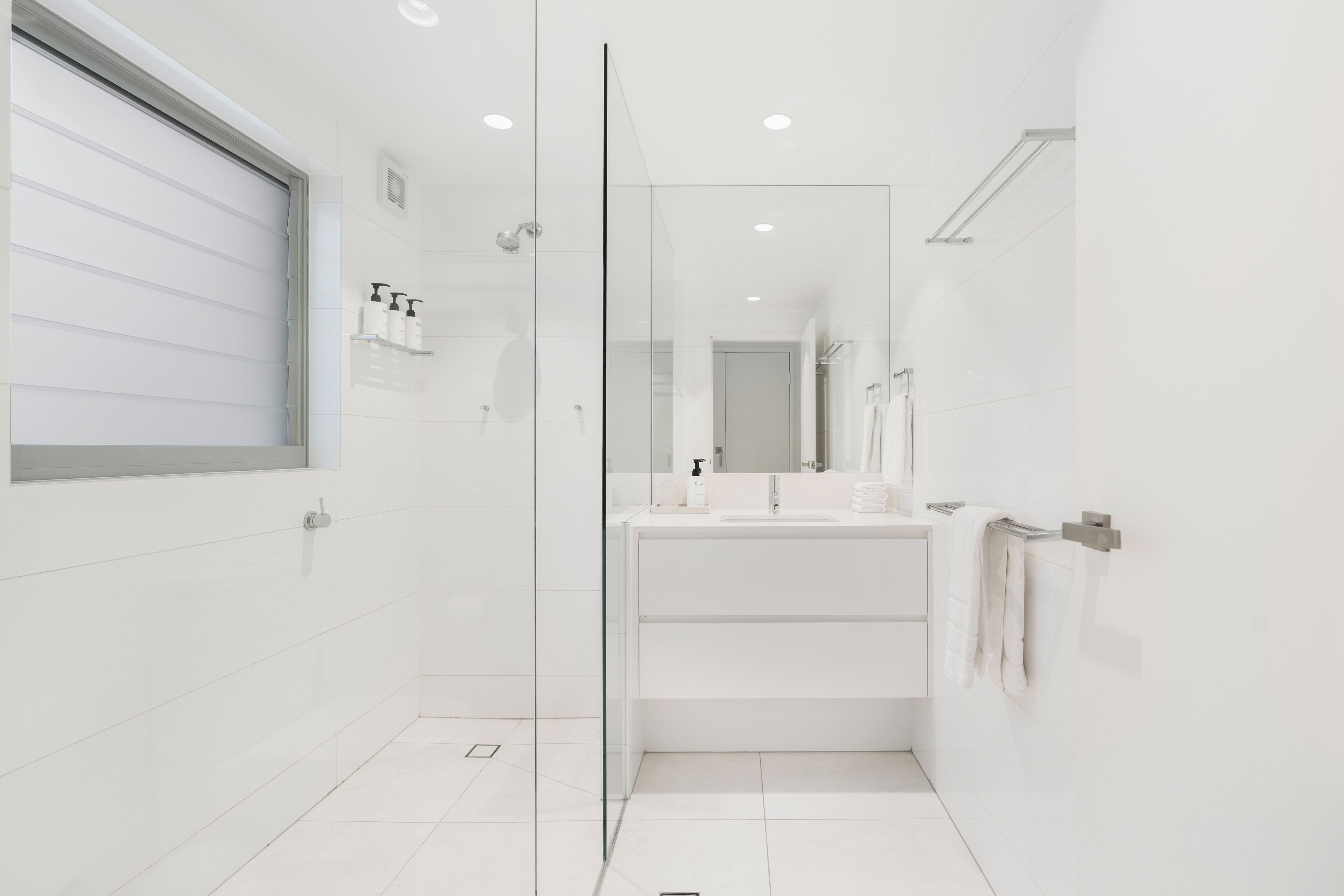 Une salle de bain moderne avec une douche à parois de verre, des carreaux blancs et un grand miroir au-dessus du lavabo.