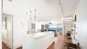 A spacious kitchen with a large island, white cabinetry, and a view of the ocean. - La Mer Noosa (Noosa Heads)