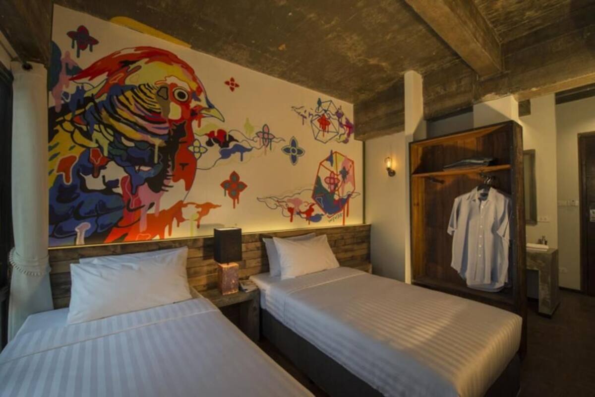 A hotel room with two beds, a large abstract painting on the wall, and a wooden wardrobe.