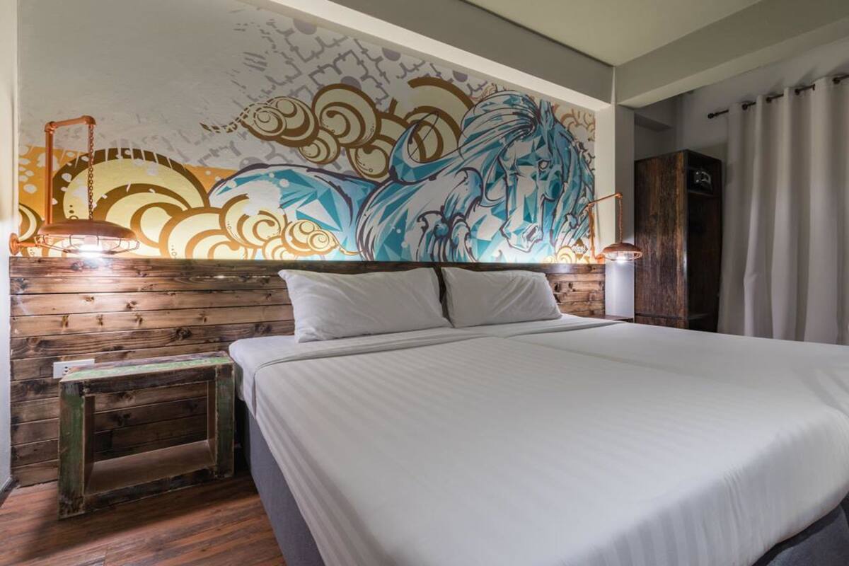 A hotel room with a large bed, wooden headboard, and a colorful mural on the wall.