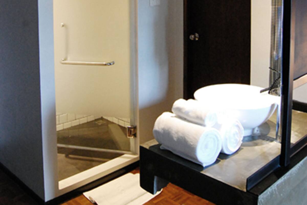 A bathroom with a glass-enclosed shower, a dark door, and a sink with towels.