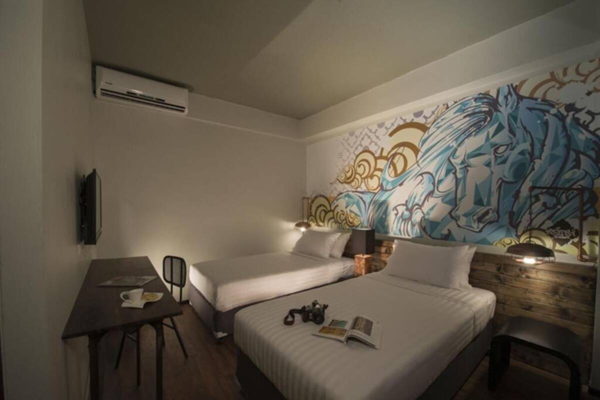 A hotel room with two beds, a desk, and a large mural on the wall.