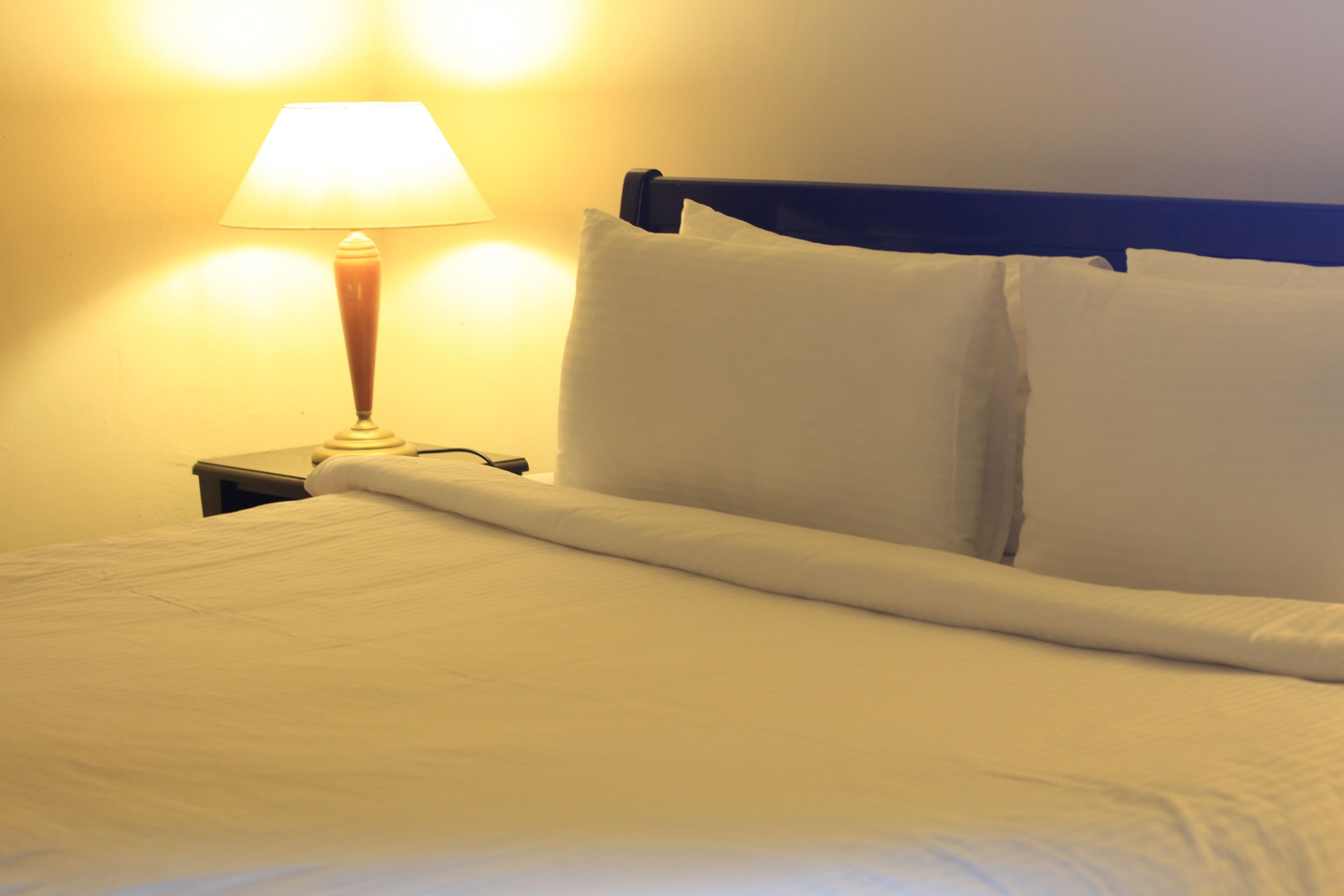 A neatly made bed with white linens, a wooden headboard, and a bedside lamp.