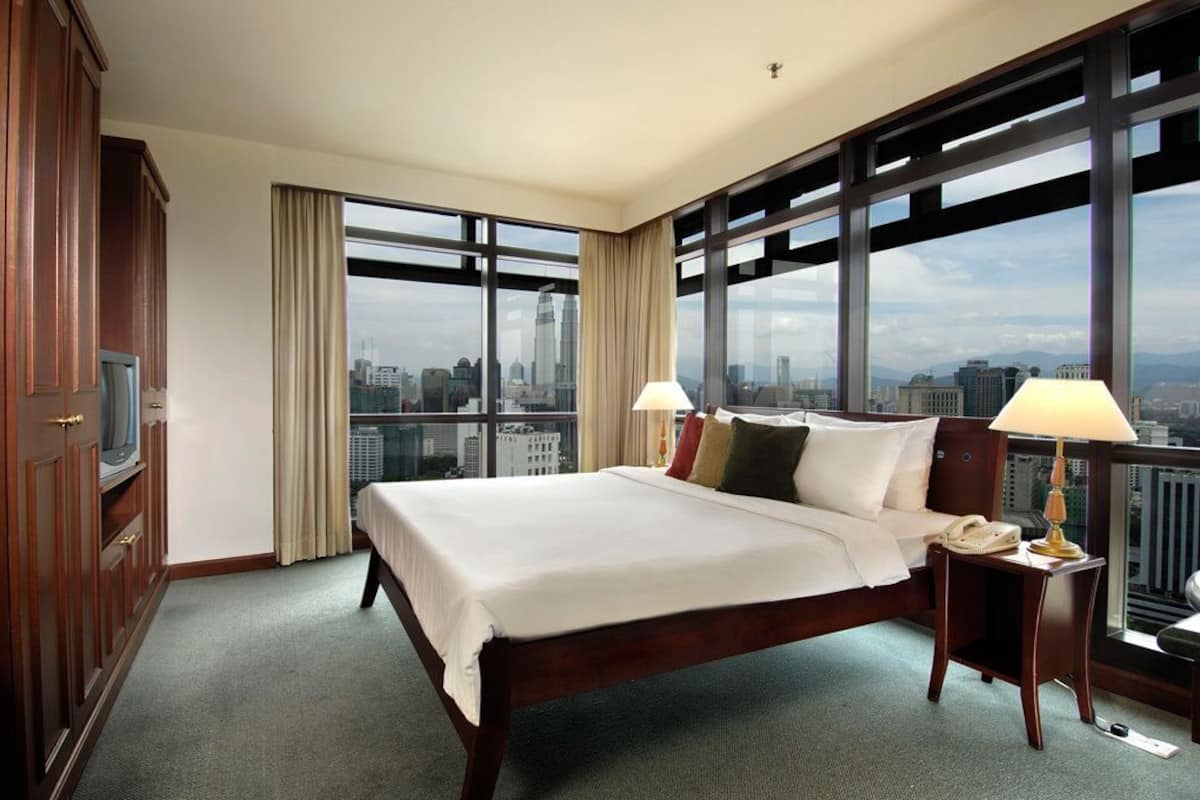 A hotel room with a large bed, a TV, a desk with a lamp, and a city view.