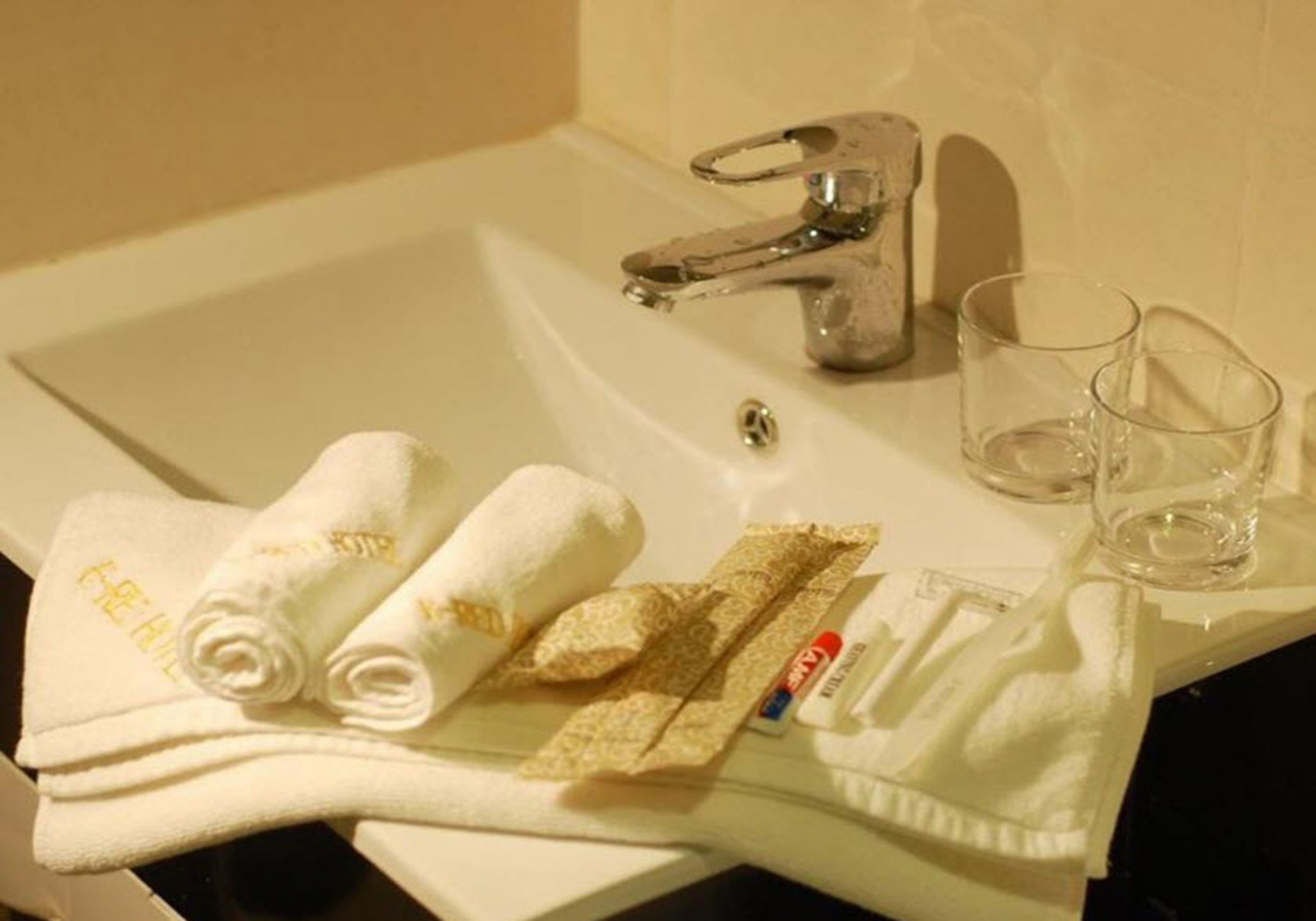 A bathroom sink with two towels, a glass, and a razor.