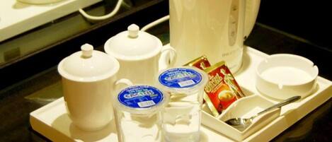 A tray with a white coffee maker, two small cups, a glass, a packet of sugar, and a spoon.