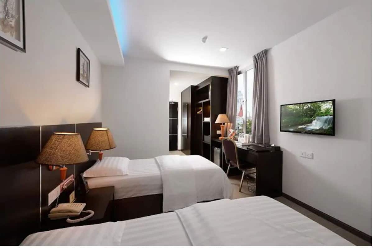 A hotel room with two beds, a desk, a chair, a television, and a phone.