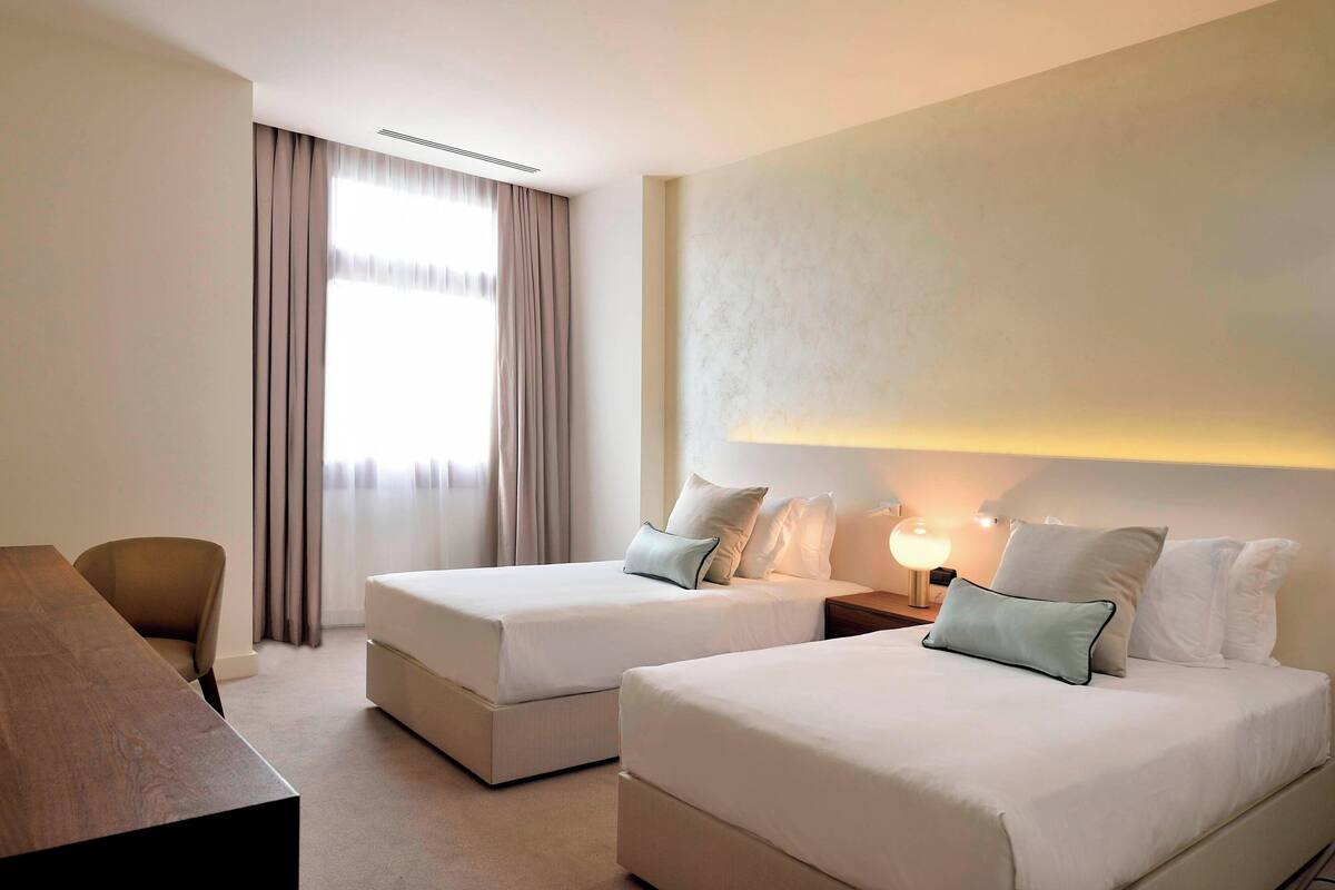 A hotel room with two beds, a desk, and a chair.