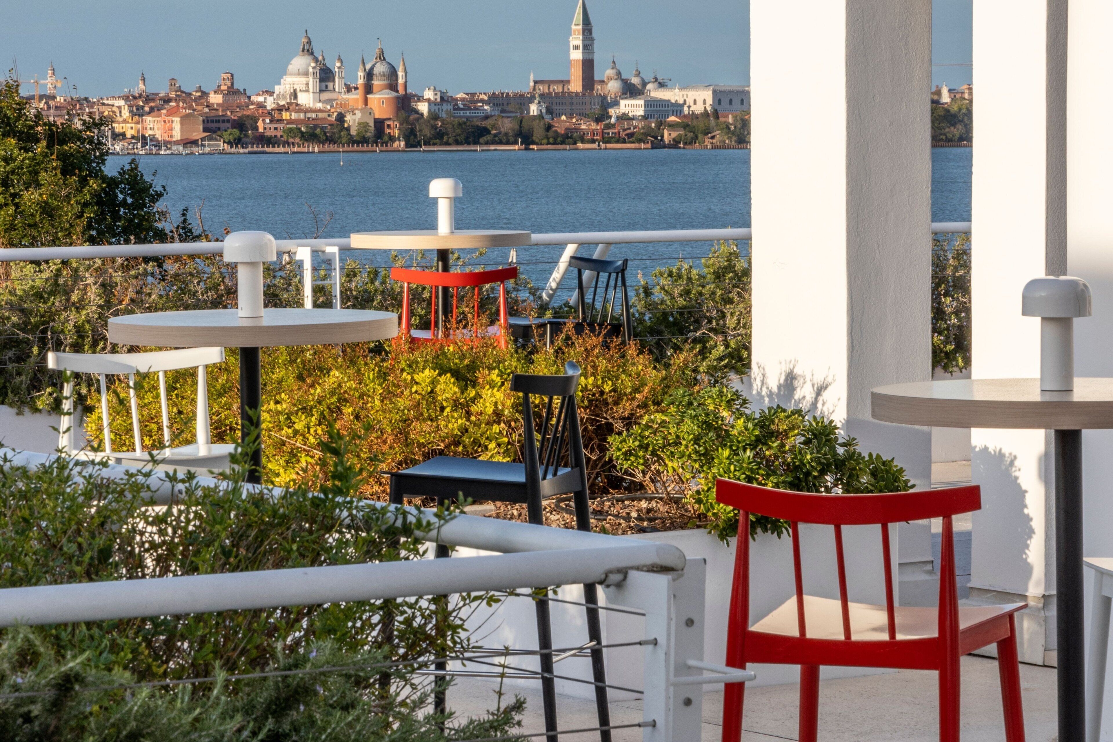 Eine Terrasse mit Tischen und Stühlen mit Blick auf ein Gewässer und eine Stadtansicht.