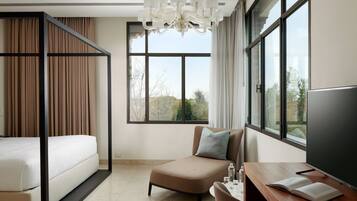 Quarto de hotel moderno com cama, sofá, escrivaninha com televisão e grandes janelas com vista para a cidade.