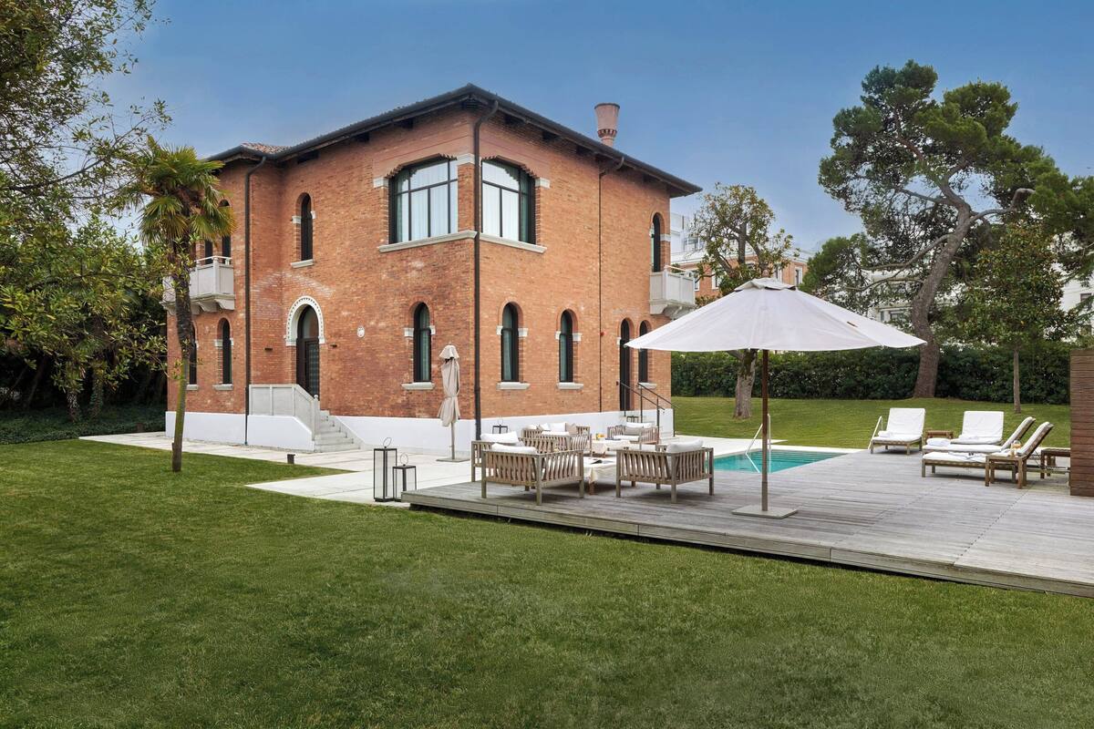 A two-story brick house with a pool, outdoor furniture, and a well-maintained lawn.