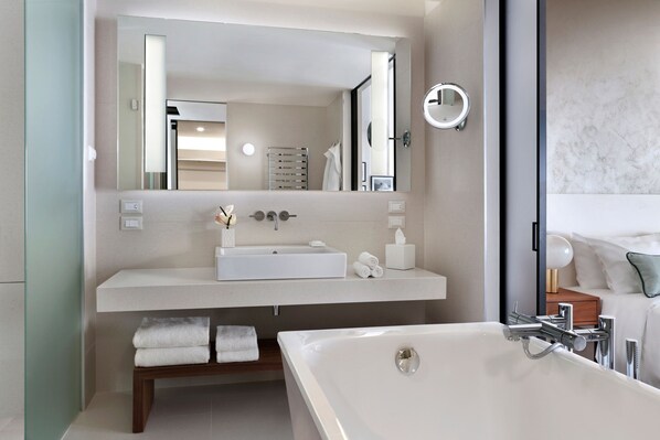 A modern bathroom with a large mirror, white sink, and bathtub. - JW Marriott Venice Resort & Spa (Venice)