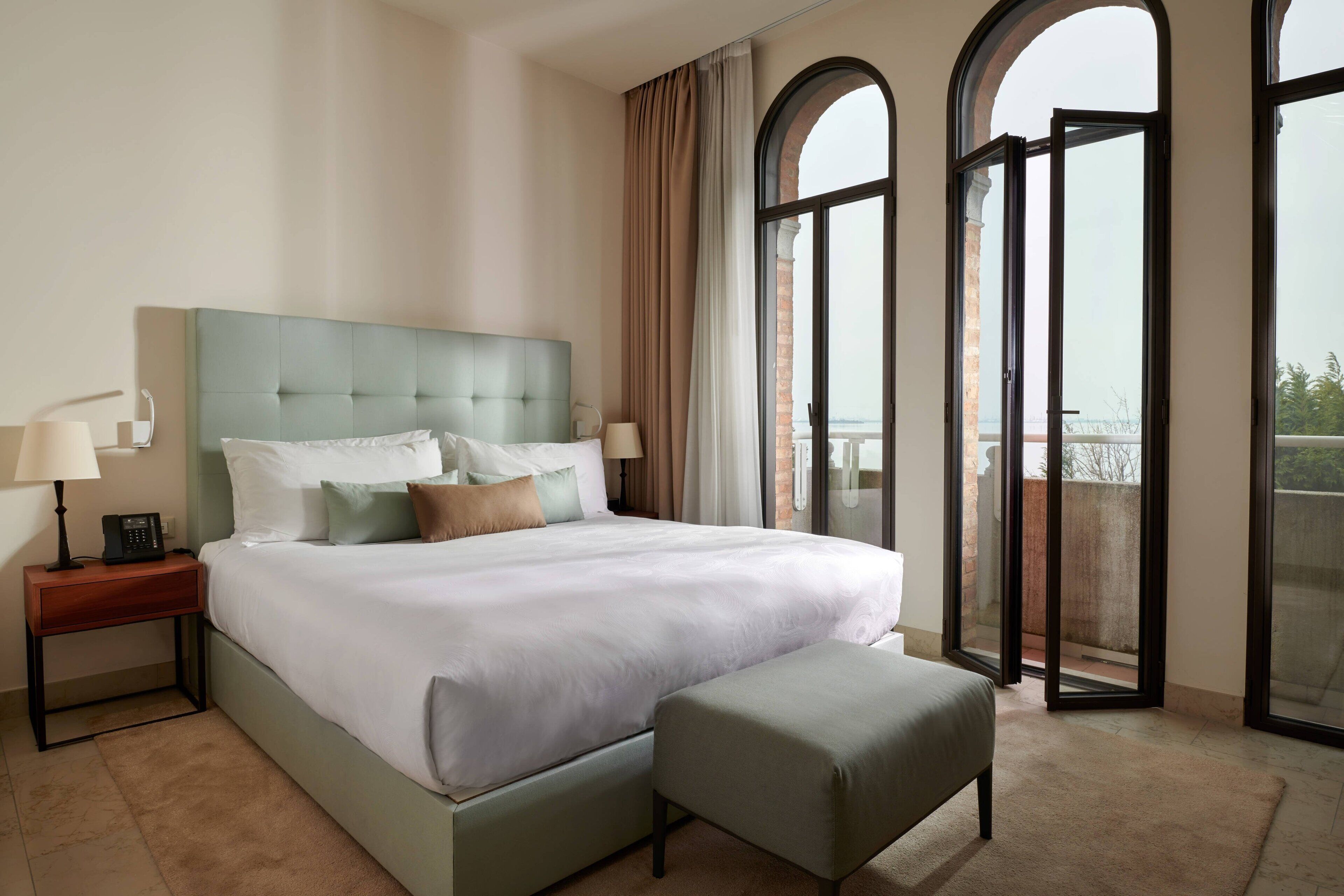 Ein modernes Hotelzimmer mit einem großen Bett, einem Nachttisch, einer Leselampe und Blick durch ein großes, rundes Fenster.