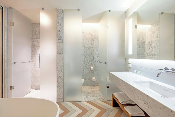 A modern bathroom with a large mirror, a bathtub, and a marble-tiled shower area. - JW Marriott Venice Resort & Spa (Venice)
