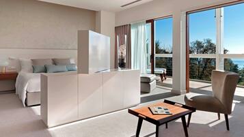 A modern hotel room with a bed, a sofa, a coffee table, and a view of the outdoors.
