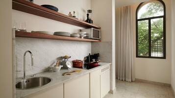 A kitchen with a marble countertop, stainless steel sink, wooden shelves, and a window with curtains.