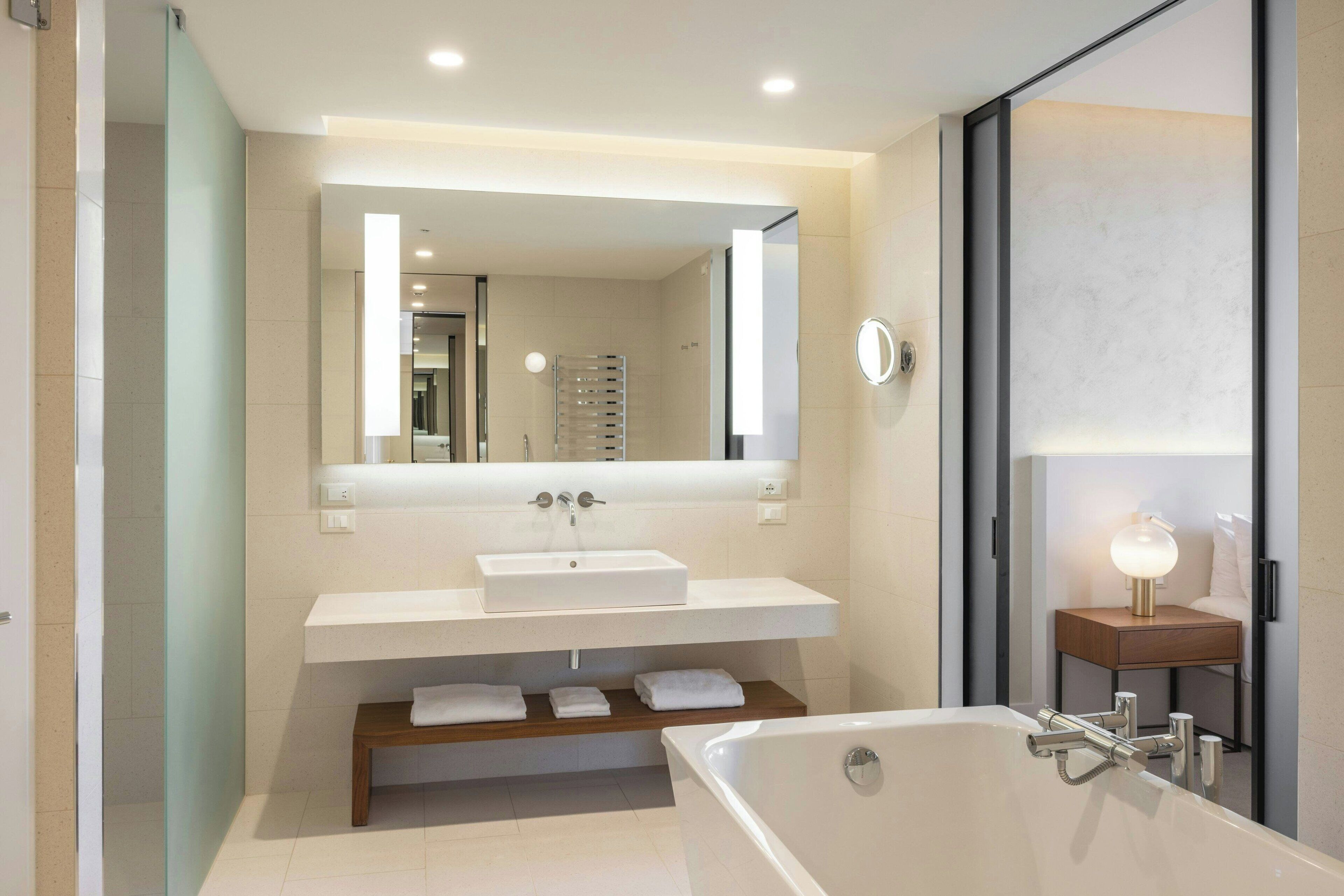Un bagno moderno con una vasca da bagno ampia, un lavandino bianco e uno specchio sopra il lavandino.