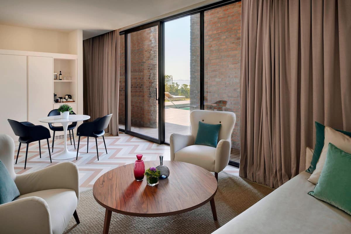 A modern hotel room with a sofa, armchair, and dining area.