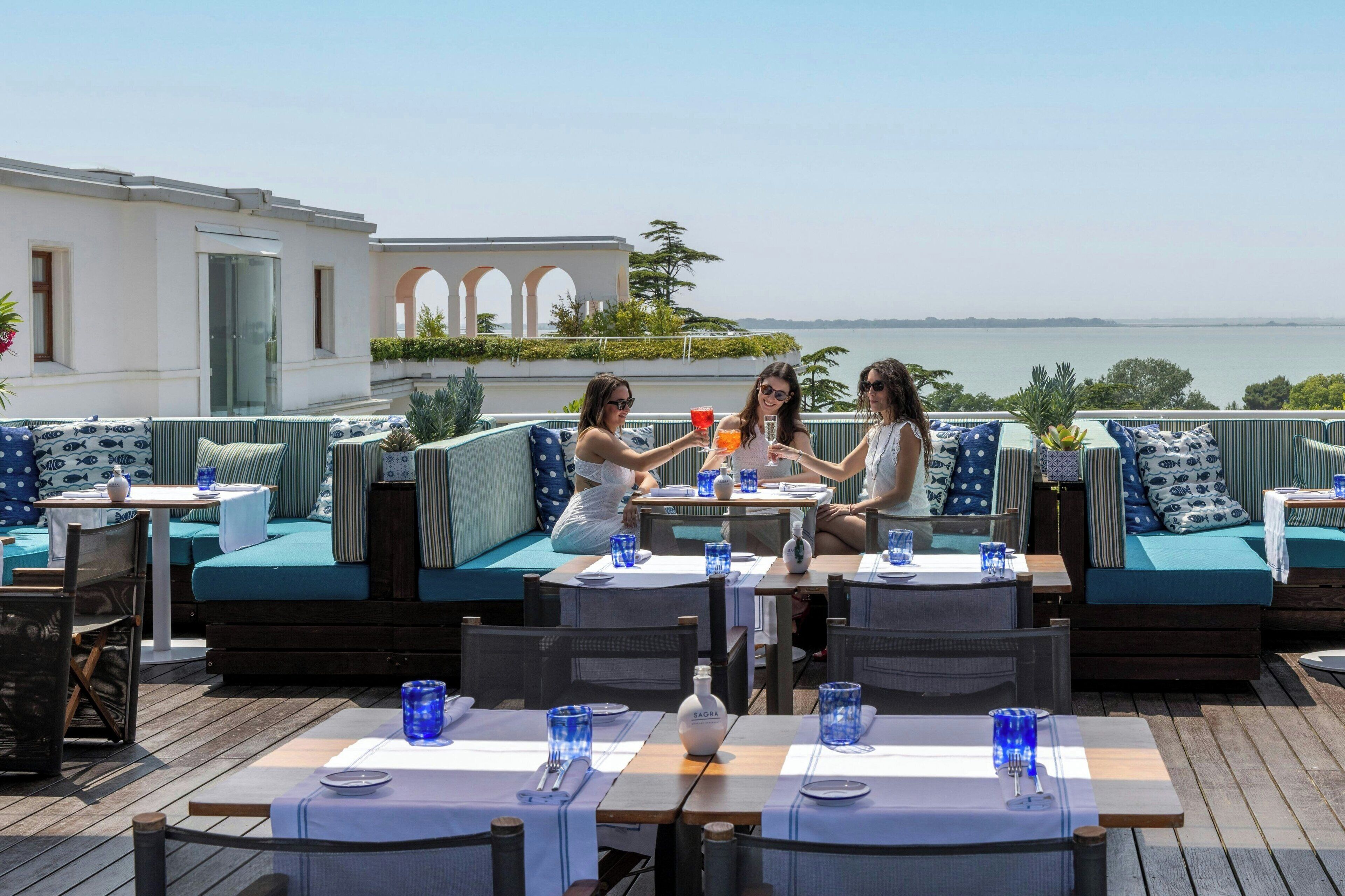 A rooftop terrace with outdoor seating and dining areas, overlooking a body of water.
