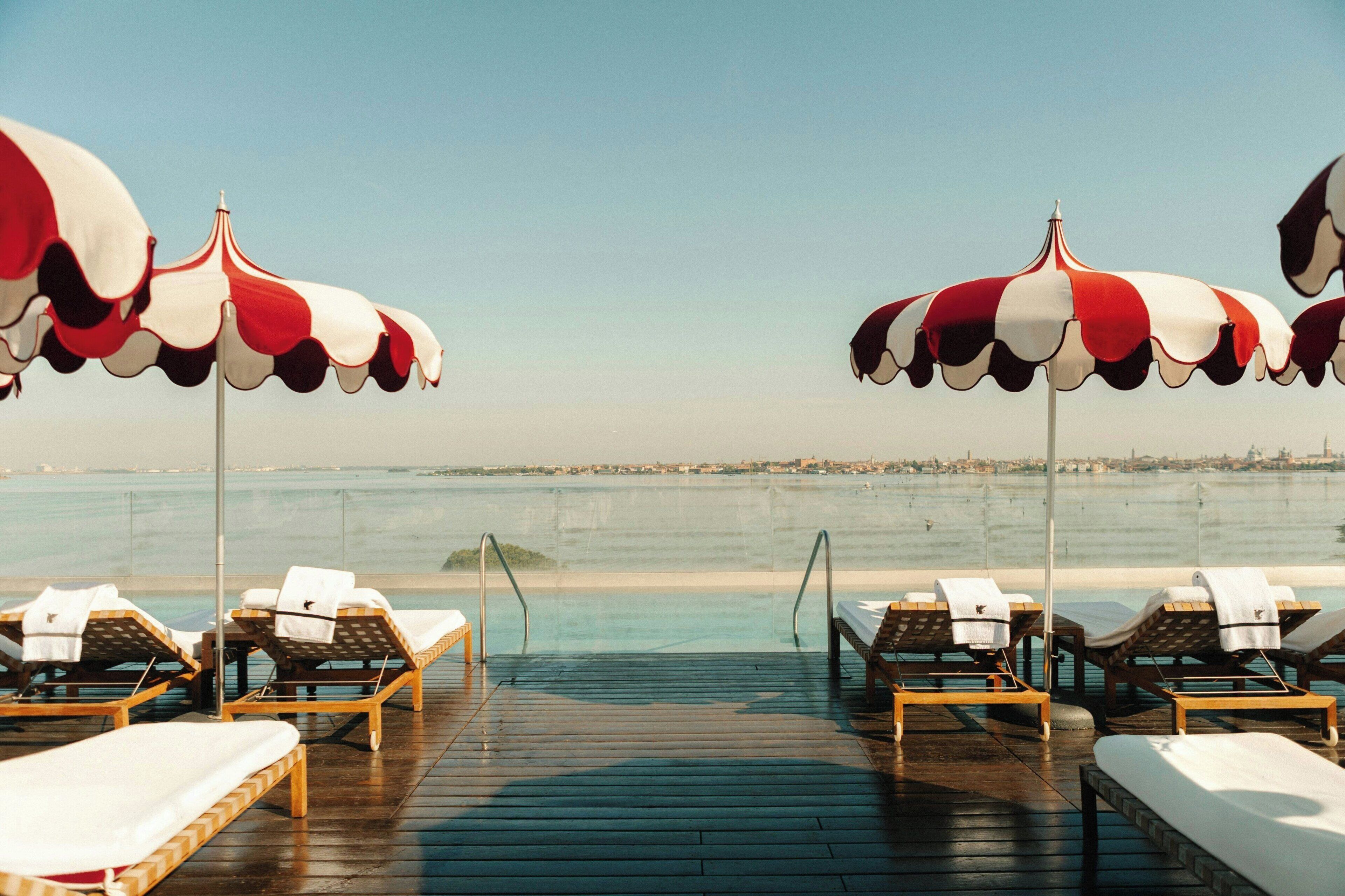 A deck with sun loungers and umbrellas overlooking a calm body of water.