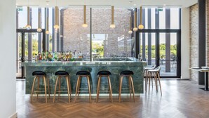 A modern bar area with a marble countertop, wooden stools, hanging pendant lights, and a brick wall backdrop. - JW Marriott Venice Resort & Spa (Venice)