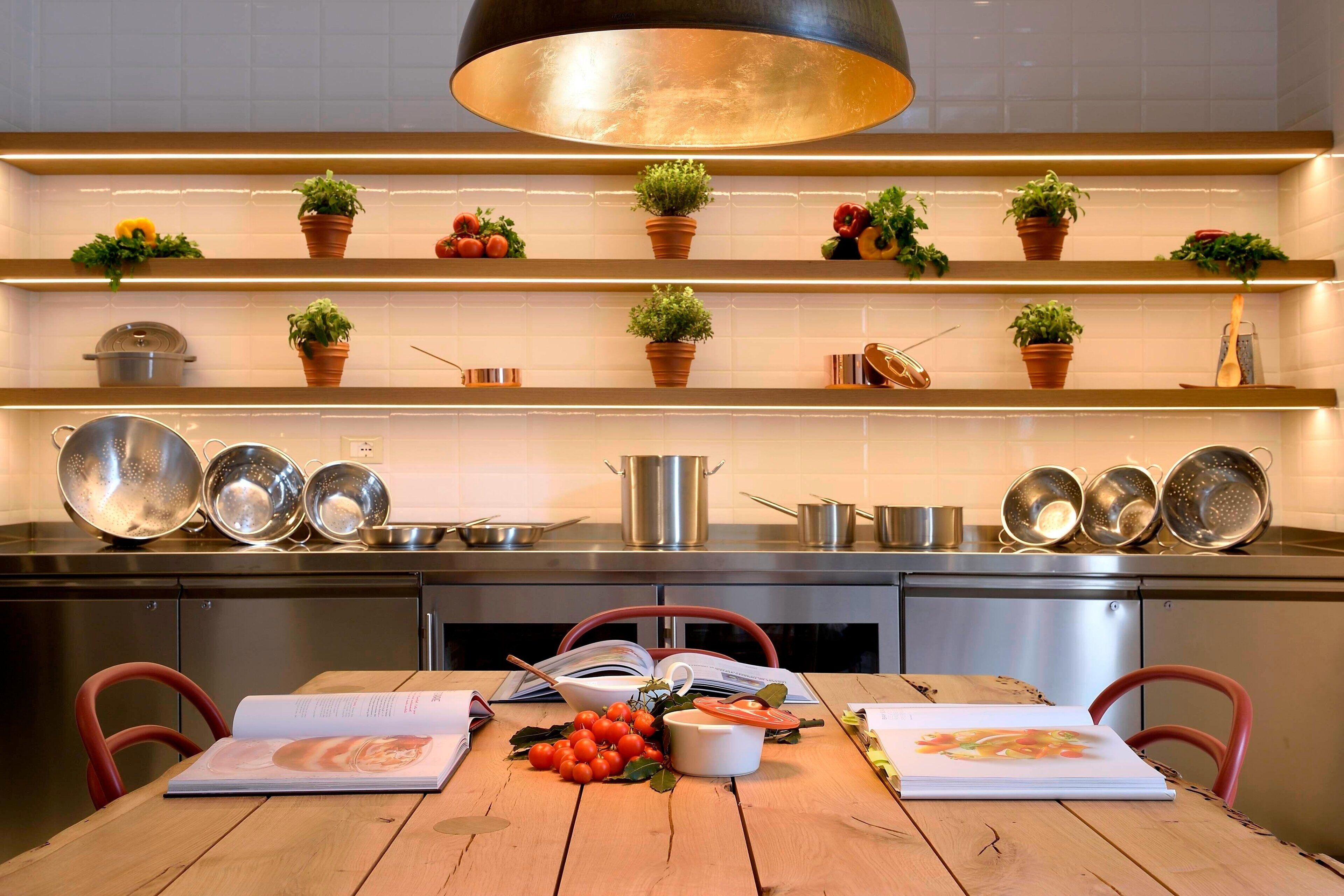 A modern kitchen with stainless steel appliances, wooden shelves with potted plants, and a wooden dining table with a book and tomatoes.
