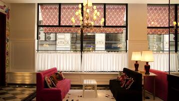 A hotel lobby with a checkered floor, two sofas, a chandelier, and patterned curtains.