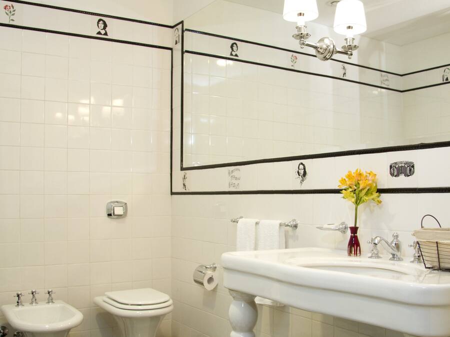 A bathroom with a checkered floor, two toilets, a bidet, a sink, and a mirror with wall-mounted lights.