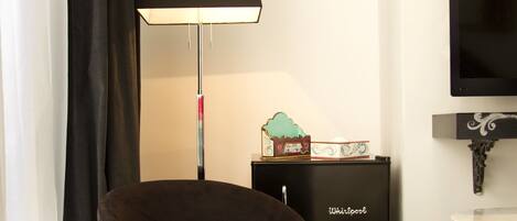 A room with a dark brown chair, a black floor lamp, a small table with a decorative item, a black cabinet labeled 'Whirlpool', and a television mounted on the wall.