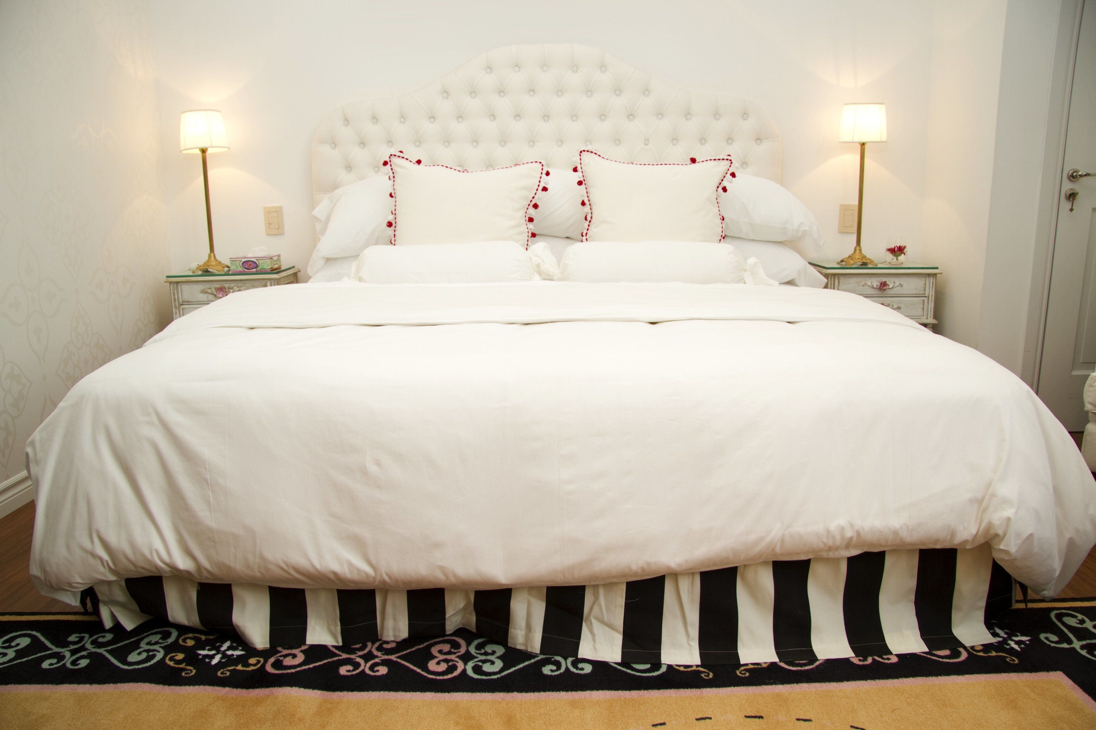 A neatly made bed with a white headboard, two bedside tables with lamps, and a patterned rug.