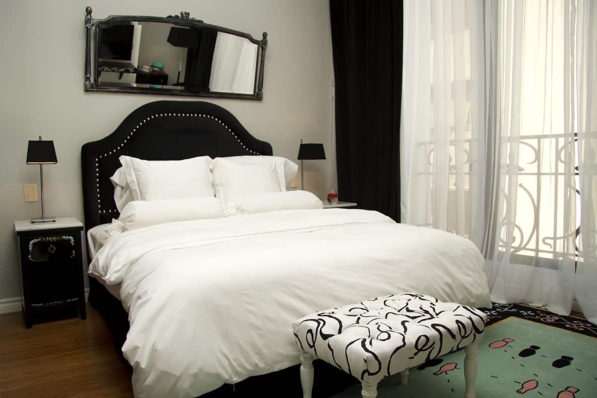 A neatly made bed with white linens, a black headboard, and a matching bench.