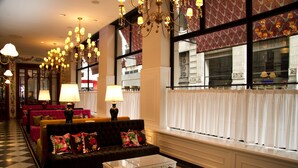 A hotel lobby with a checkered floor, a black sofa with floral cushions, a white coffee table, and multiple chandeliers. - Tango de Mayo Hotel (Buenos Aires)