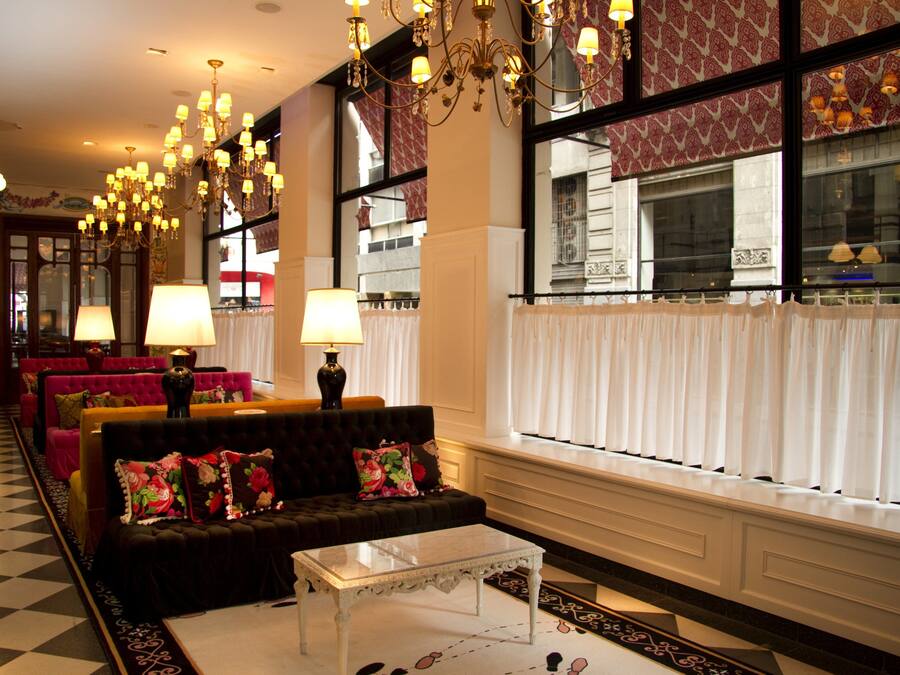 Een hotellobby met een zwart-wit geruite vloer, een zwarte bank met bloemkussens, een witte bijzettafel en meerdere kroonluchters.