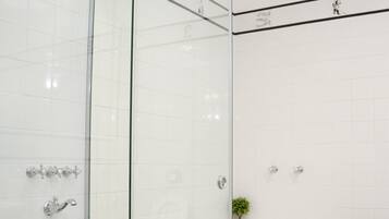 A modern bathroom with a glass shower enclosure, a white bathtub, and a checkered floor.
