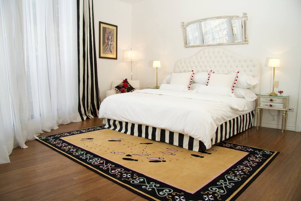 A neatly arranged bedroom with a large bed, two bedside tables, and a decorative rug.