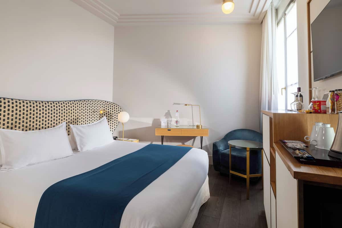 Habitación de hotel con una cama bien hecha, un escritorio con lámpara, una silla y un televisor en la pared.