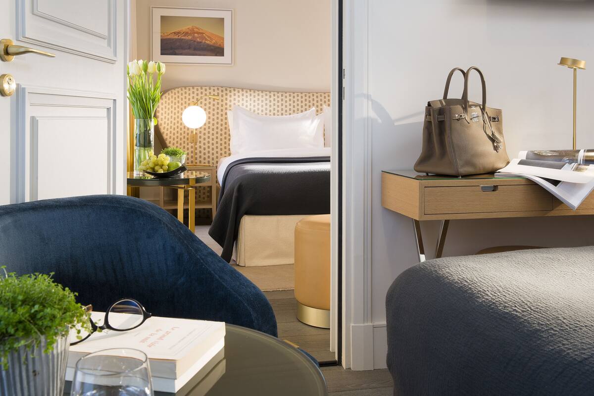 Una habitación de hotel con cama, mesita de noche, lámpara y un bolso grande sobre la mesita.