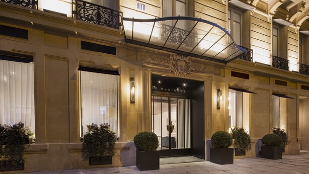A hotel entrance with a wrought iron balcony, large windows, and potted plants. - Hôtel Le Marianne (Paris)