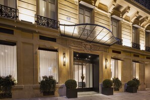A hotel entrance with a wrought iron balcony, large windows, and potted plants. - Hôtel Le Marianne (Paris)