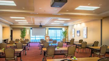 A conference room with multiple tables and chairs, a projector, and a large screen.