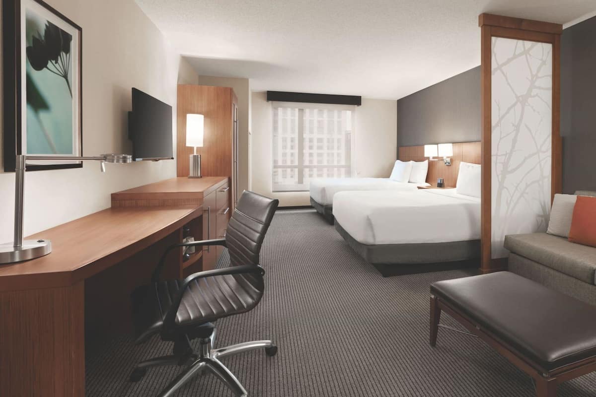 Ein Hotelzimmer mit Schreibtisch, zwei Betten, einer Couch und einem Fernseher.