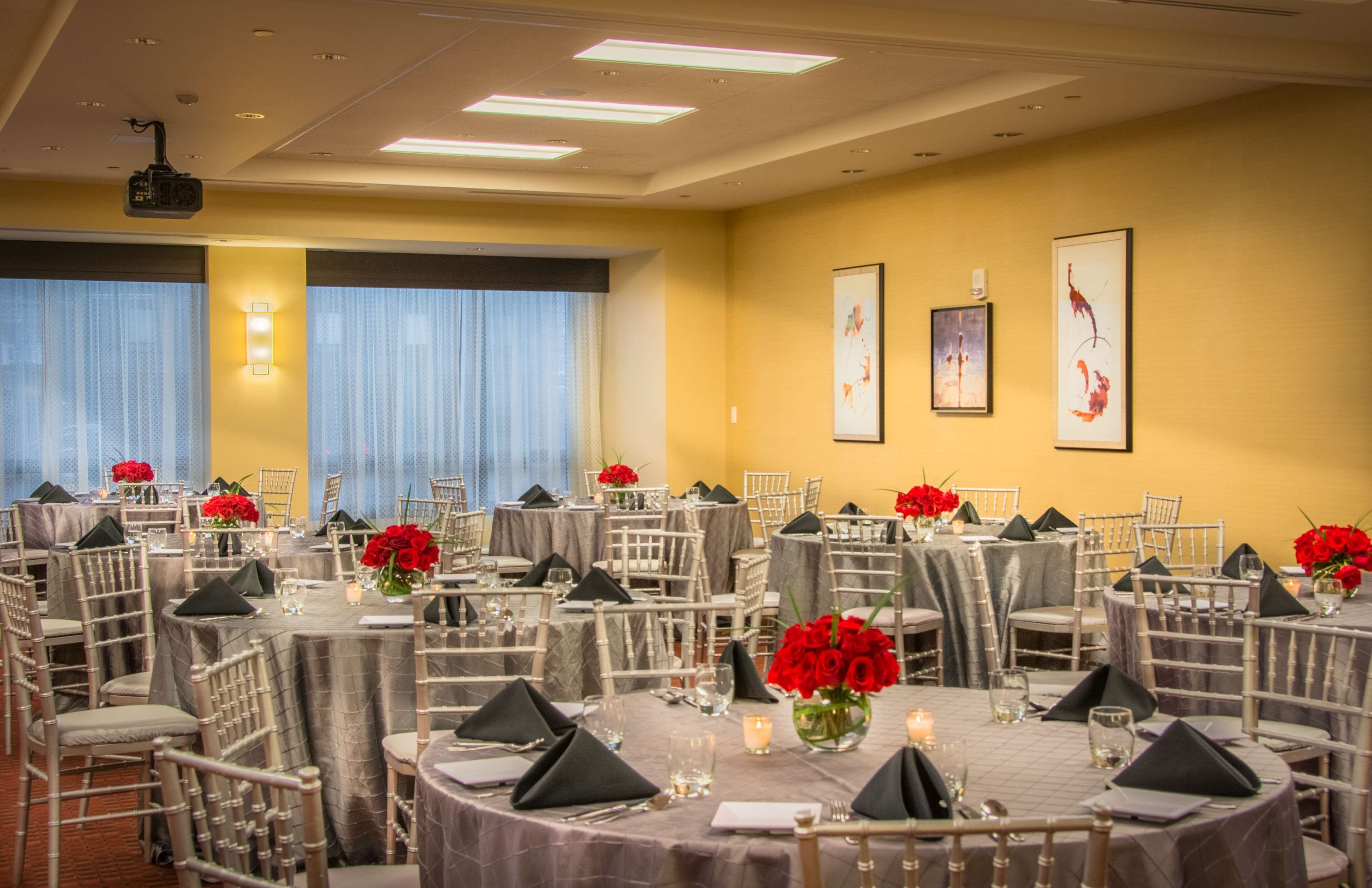 A conference room with round tables, chairs, and red flowers.