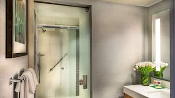 A modern bathroom with a glass shower enclosure, a white sink, and a mirror with a vase of white flowers.