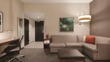 A modern hotel room with a desk, office chair, sofa, and ottoman.