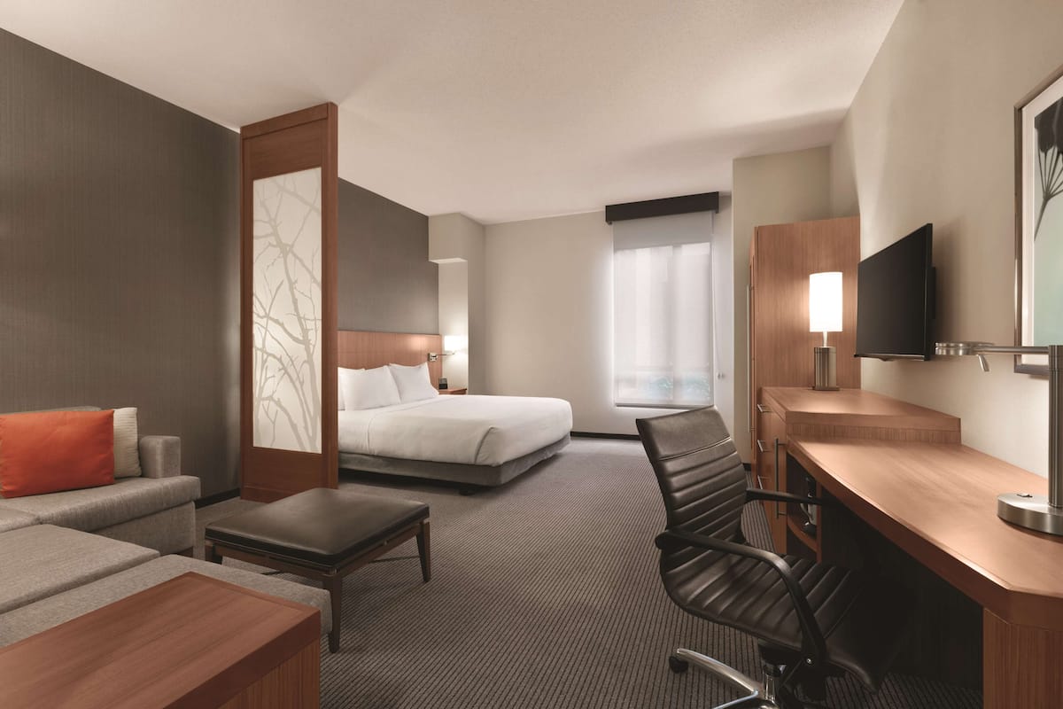 Ein Hotelzimmer mit Bett, Schreibtisch, Sessel, Sofa und Fernseher.