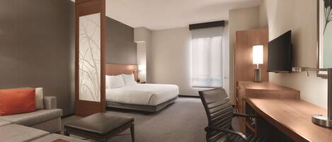 A hotel room with a bed, a desk, a chair, a sofa, and a television.